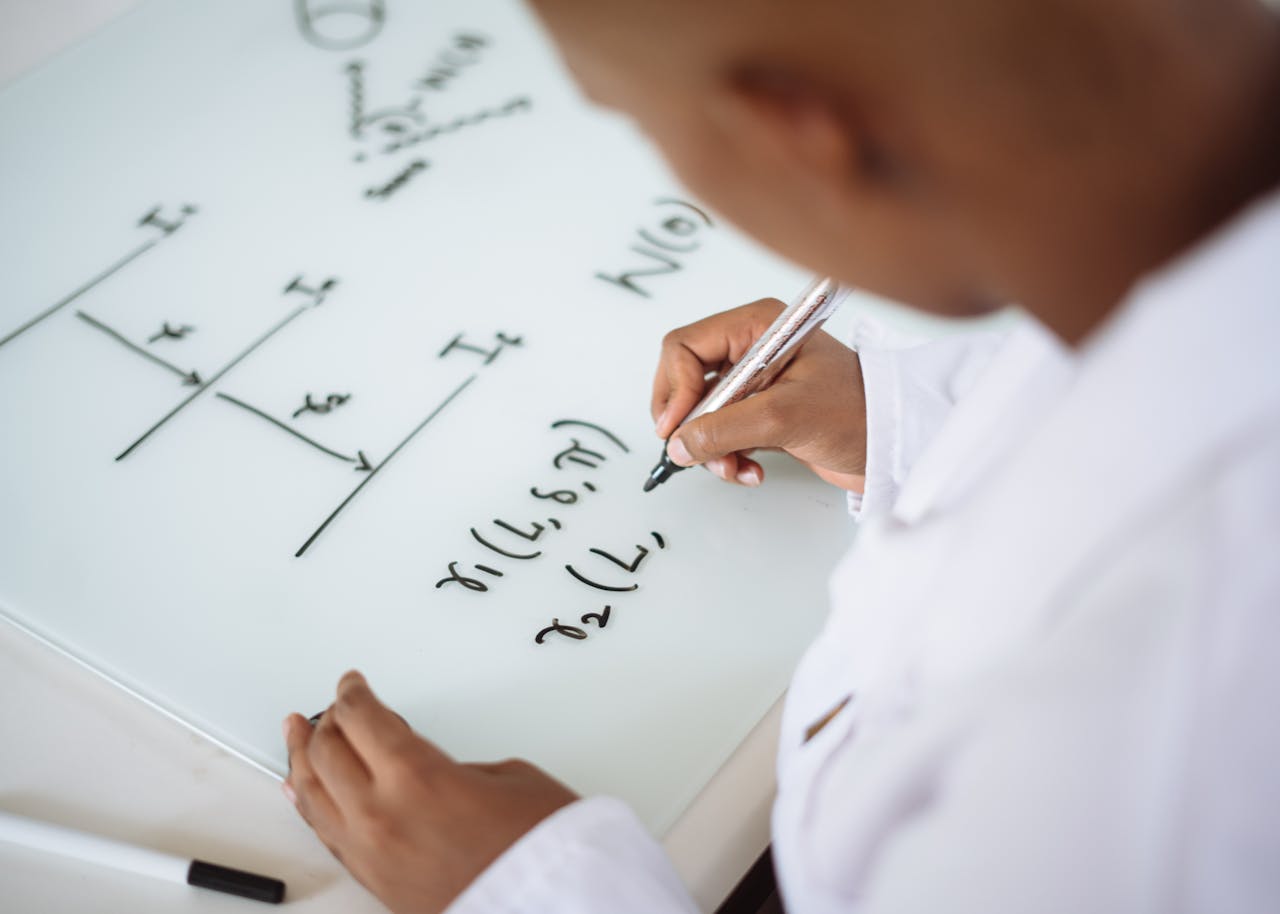 who-we-are From above anonymous ethnic student wearing uniform and solving problem in chemistry while writing formula on white table in lab